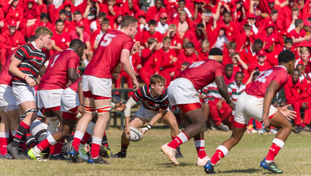 Surrounded by a sea of KES red on all sides, scrumhalf Rhett Quinn clears the ball from ruck. (Captain Sasha Kadira crashes over for a try, with Colm Reardon (left) and Luyanda Kunene (right) celebrating the score, too. In the background, Basher Ridge explodes with joy. (Photo: Justin Waldman Sports Photography)